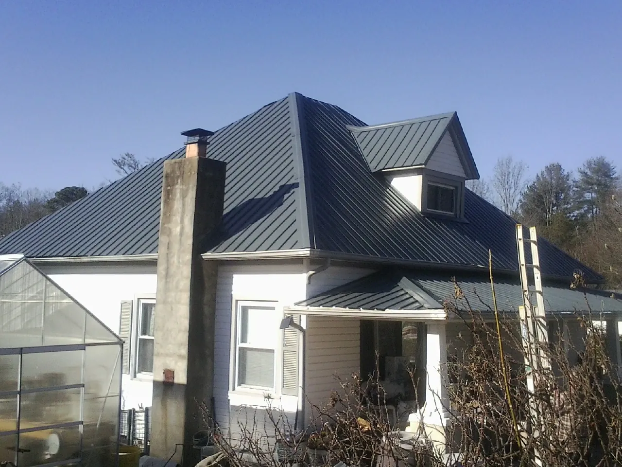 Dark blue standing seam metal roof on a white farmhouse with dormer — Slate & Tile Roof Repair by Roofing Brothers in La Porte City