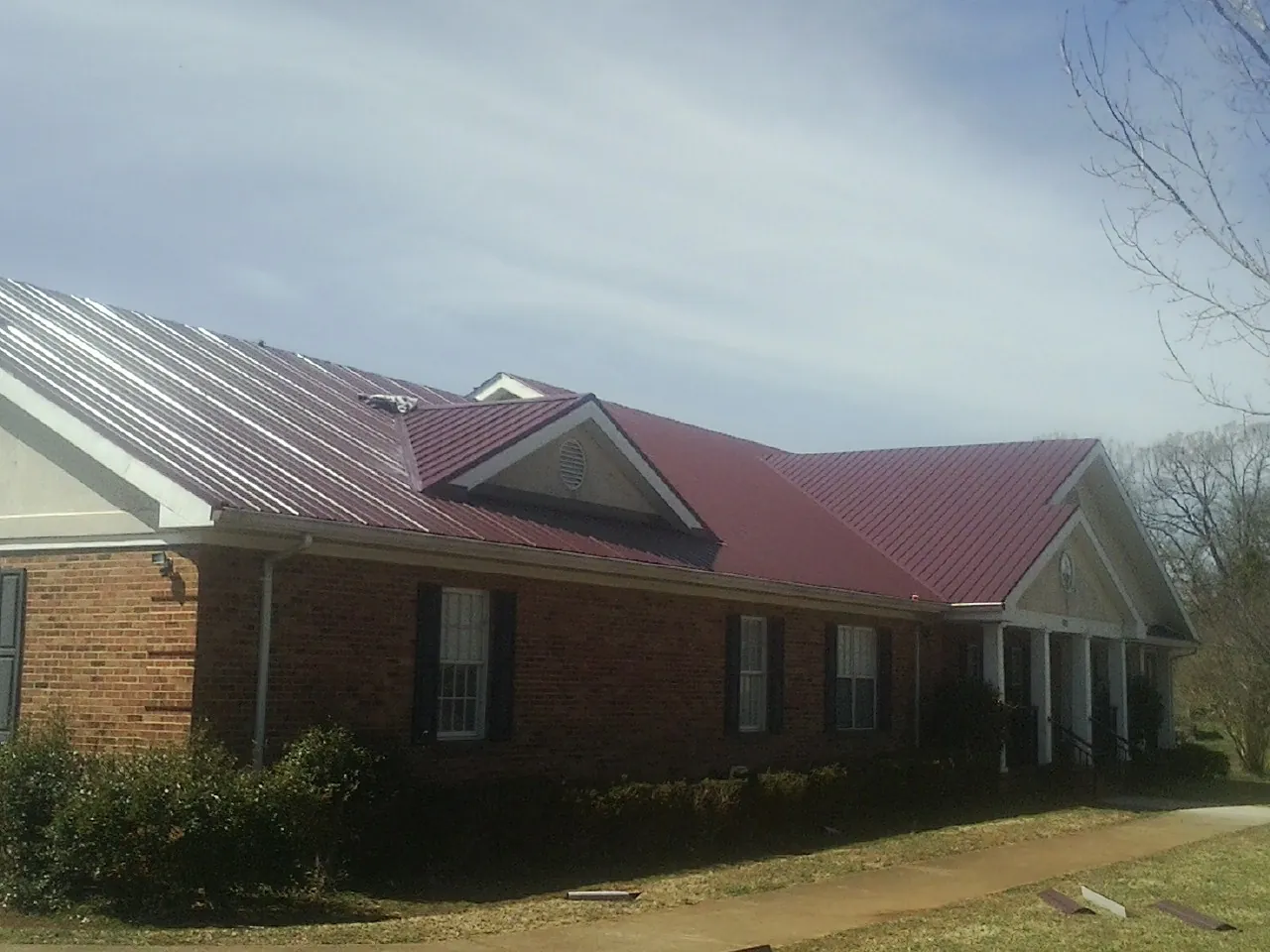 Red metal roof with gabled entries on a long brick building, from a Hail Damage Roof Repair job in La Porte City