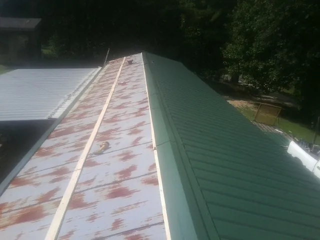 Old rusted panels beside newly installed green metal roofing — Wind Damage Roof Repair by Roofing Brothers in La Porte City