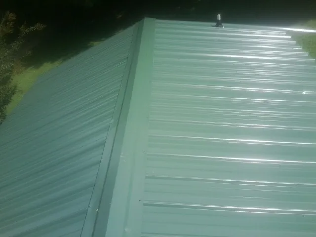 New green metal panels meeting at the ridge of a roof — Flat Roof Repair work by our crew in La Porte City