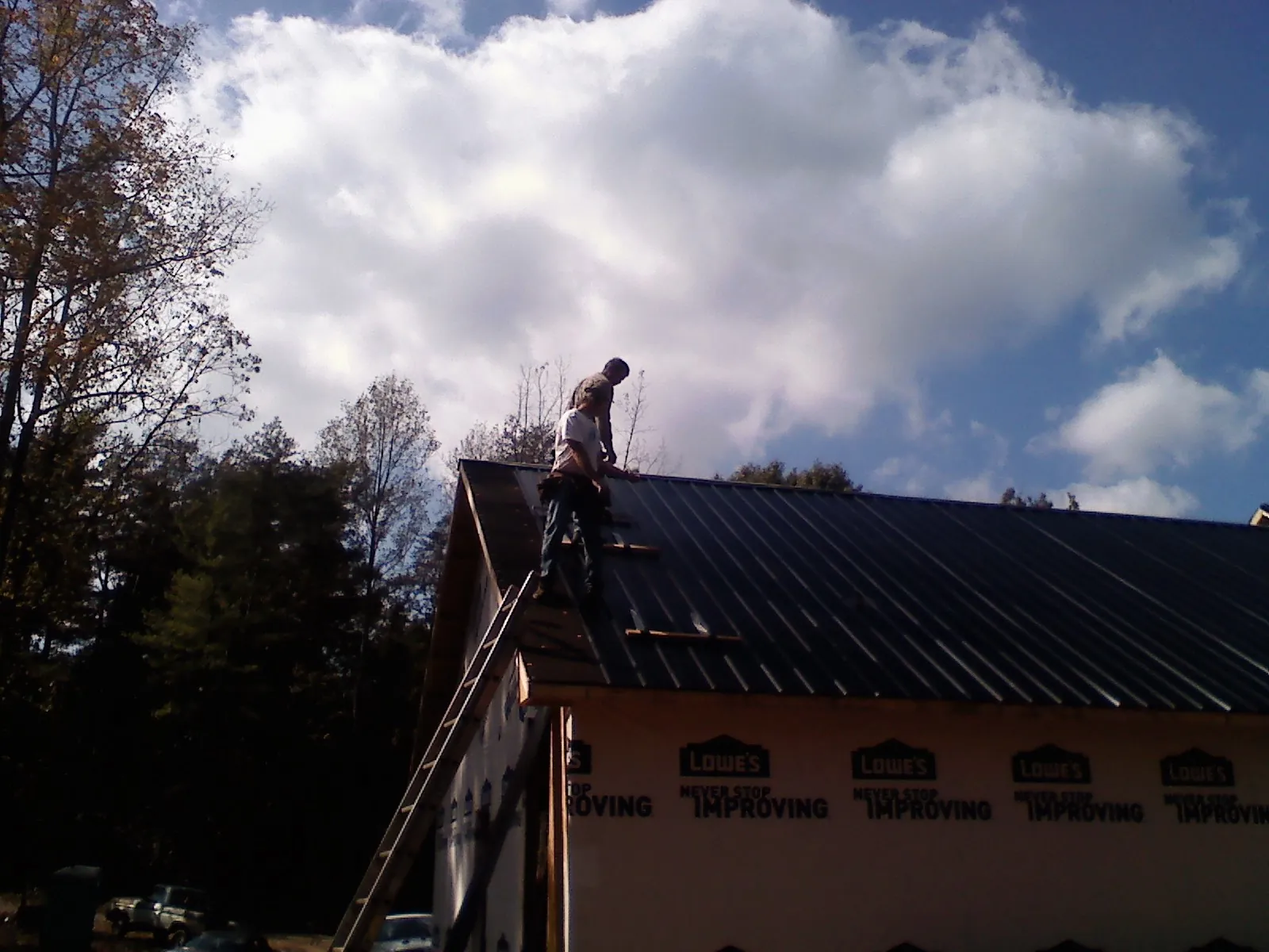 Roofer fastening dark metal panels high against a cloudy sky, from a Roof Inspection job in La Porte City