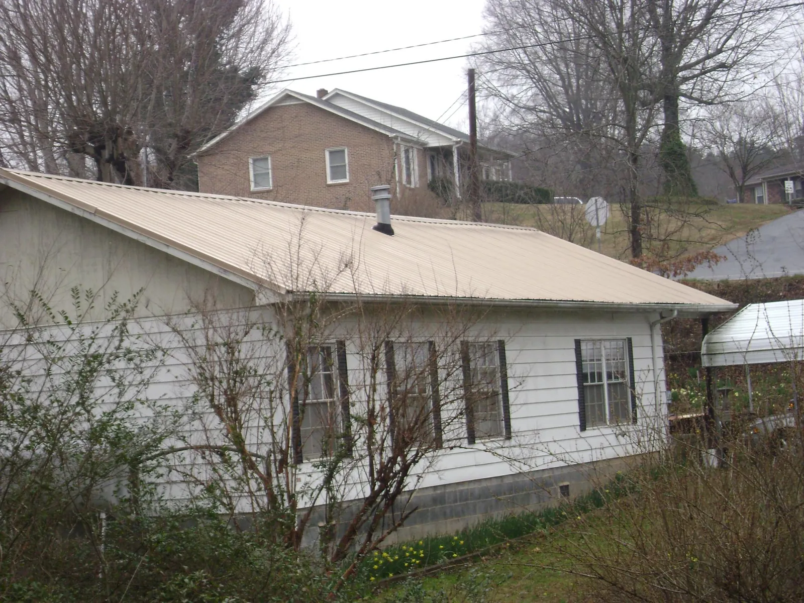 Tan metal roof on a white sided house set into a hillside — Commercial Roofing by Roofing Brothers in La Porte City