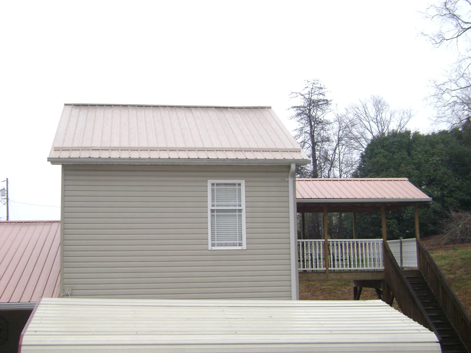 Tan metal roofs on a two story addition and attached porch, from a Roof Replacement job in La Porte City